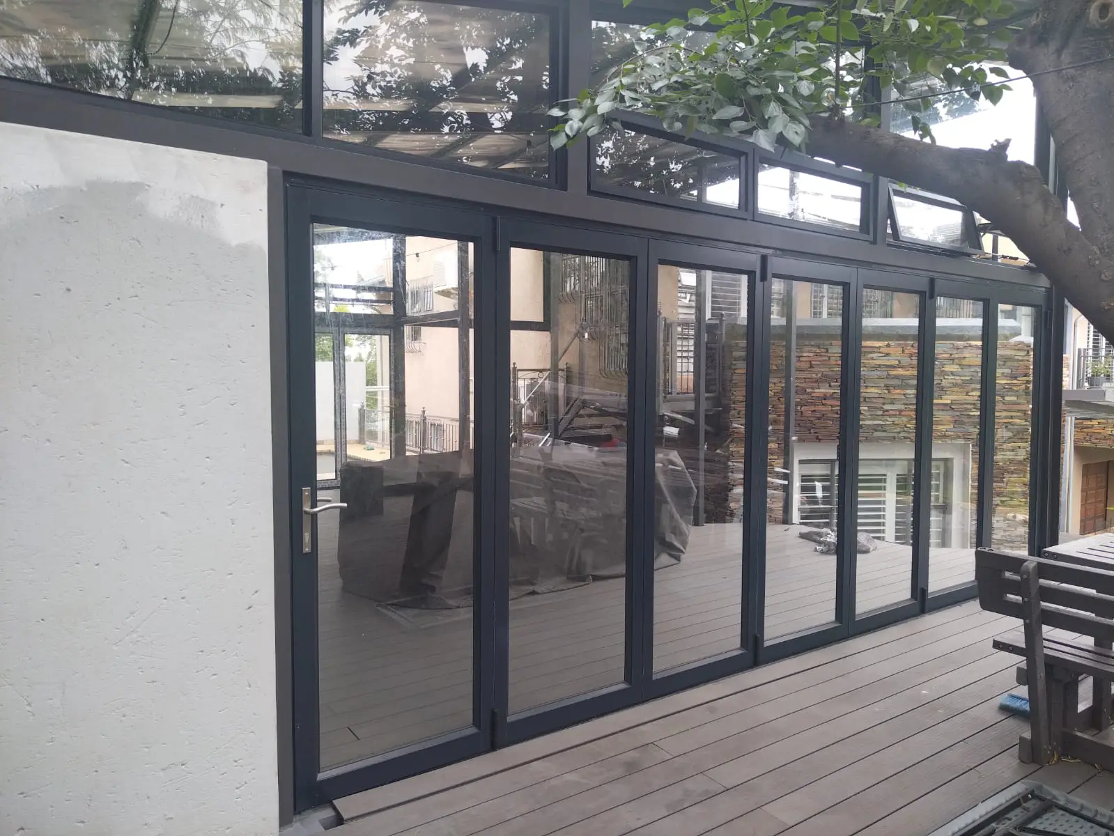 Black aluminium folding doors across a timber deck beneath trees