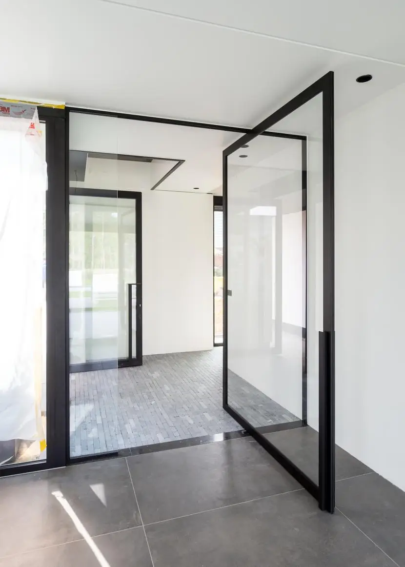 A black aluminium pivot door standing open in a bright interior